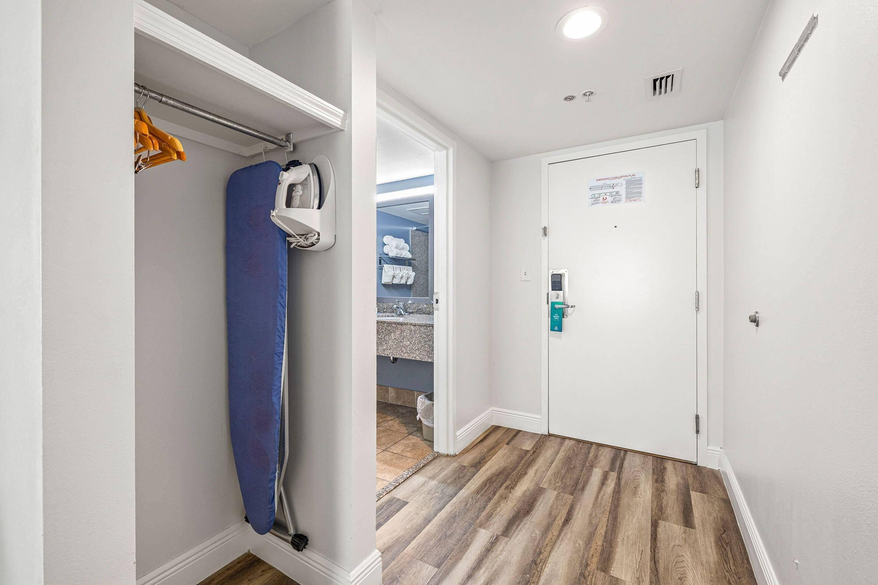 Un pasillo con suelo de madera, una puerta blanca con un letrero verde y una cortina de ducha azul.