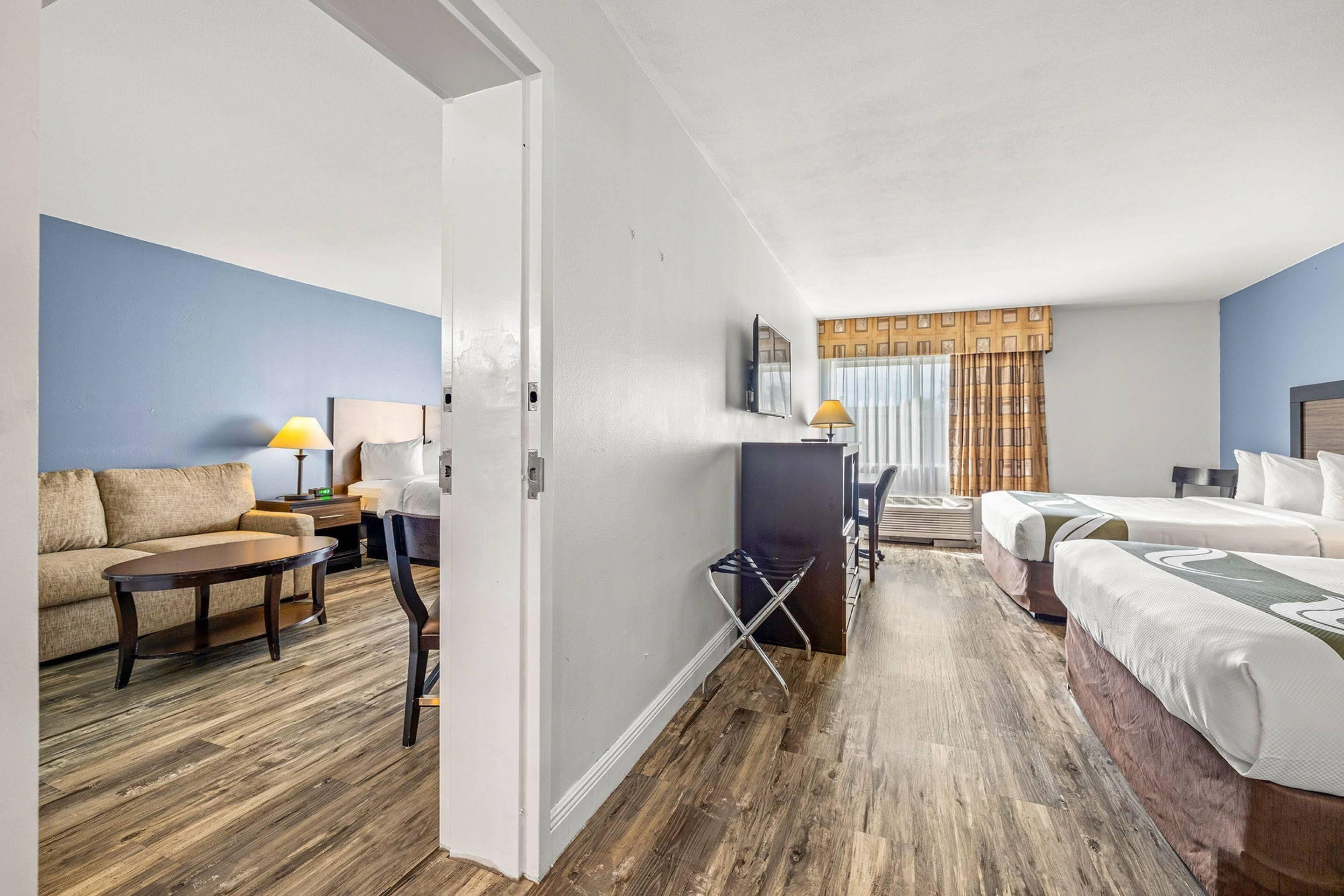 A hotel room with a sofa, two beds, a desk, and a chair.