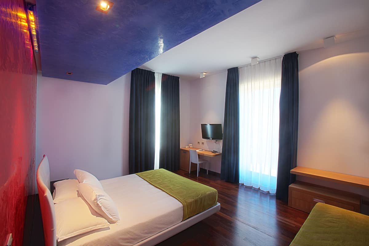 A hotel room with a bed, a desk, a chair, a TV, and a window with curtains.