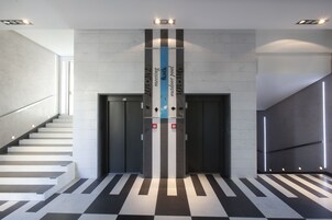 Un ascensor moderno con diseño a rayas y botones de emergencia, rodeado por una escalera y un suelo con diseño de cuadros.
