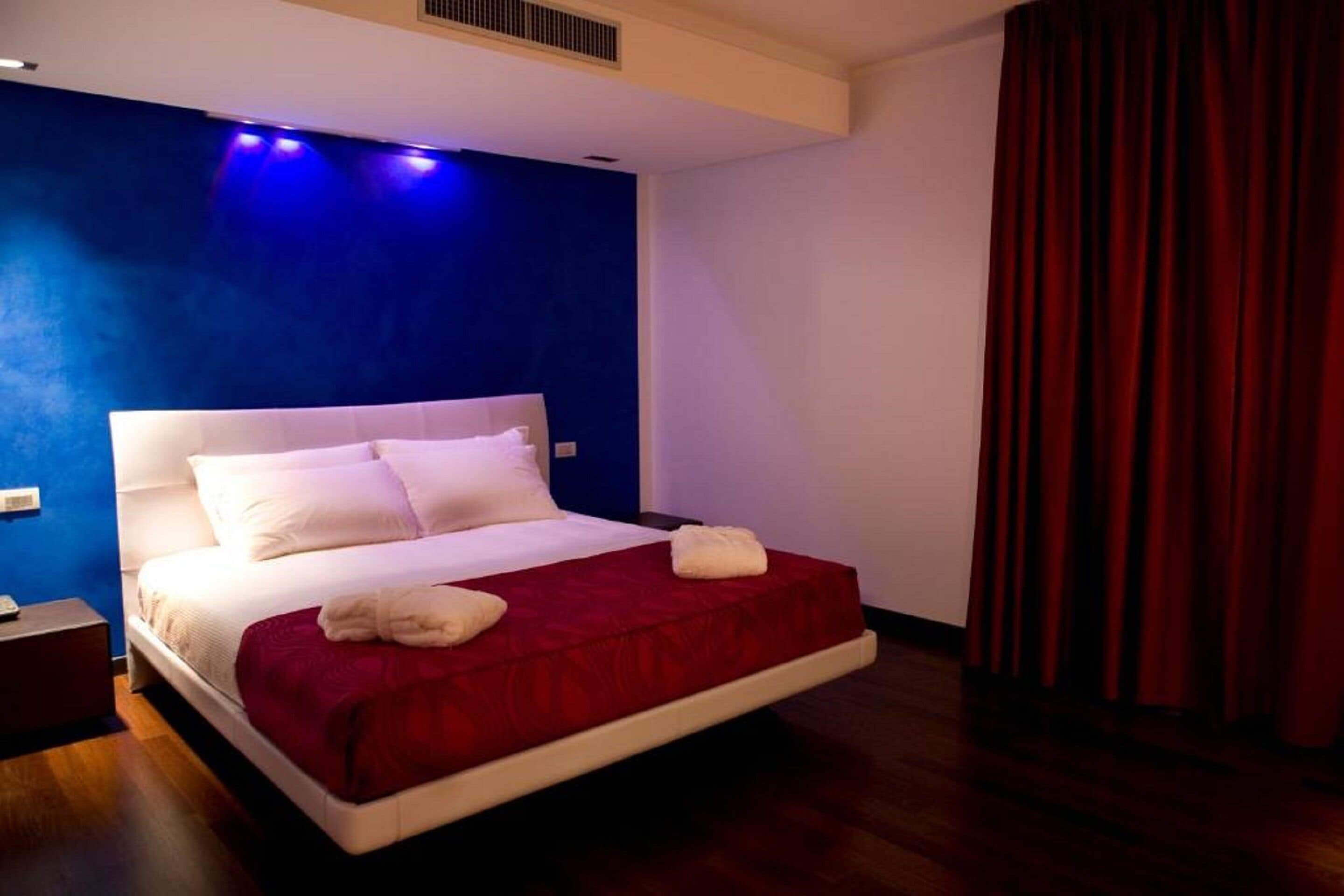 A hotel room with a large bed, a red throw blanket, white pillows, and a red curtain.
