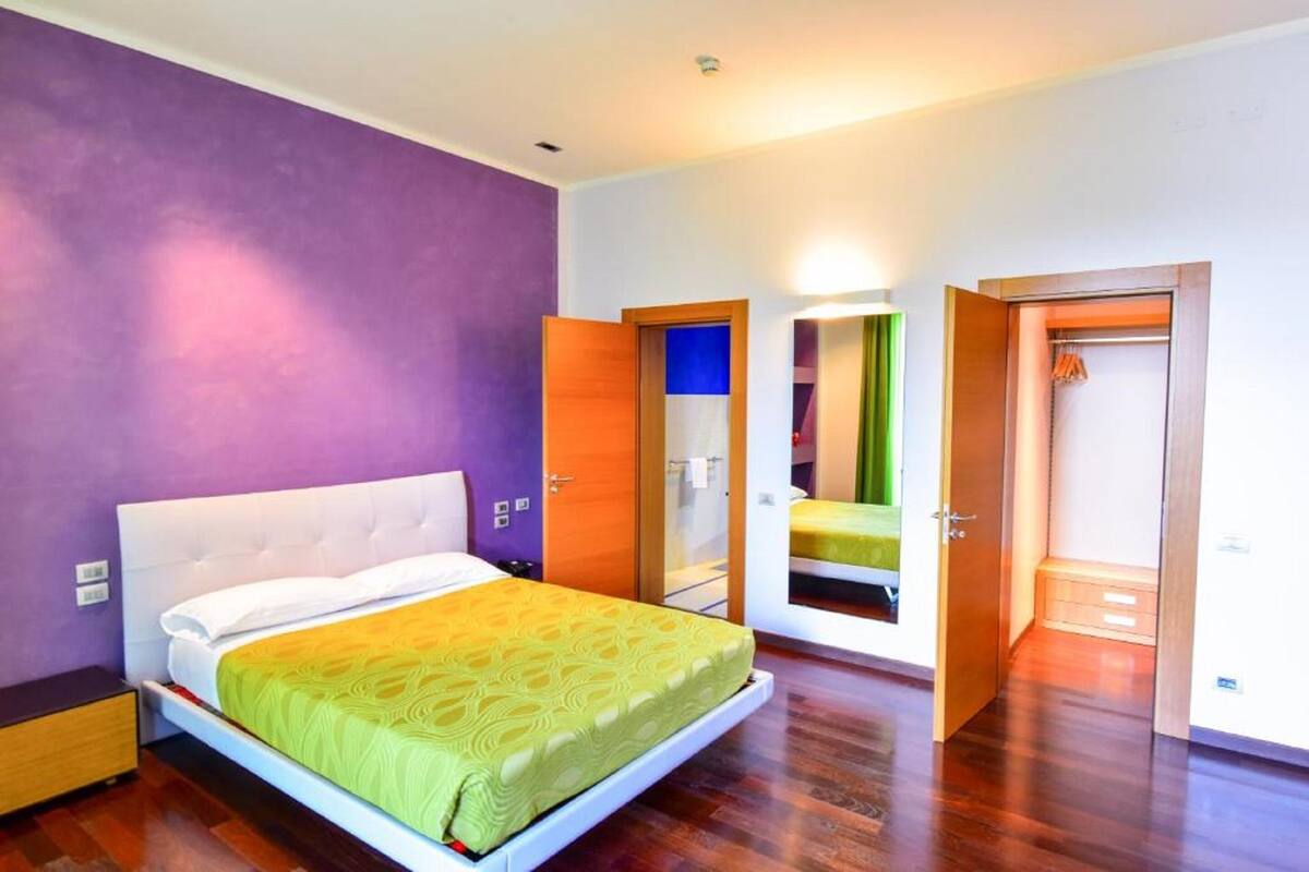 A modern bedroom with a large bed, a wardrobe, and a mirror.