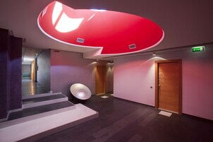 Un pasillo moderno con un llamativo techo rojo, una lámpara esférica y una escalera que lleva a un ascensor.