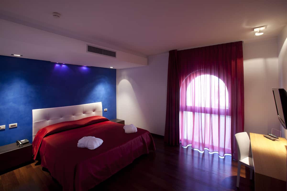 A hotel room with a large bed, a desk with a chair, a TV, and a window with curtains.