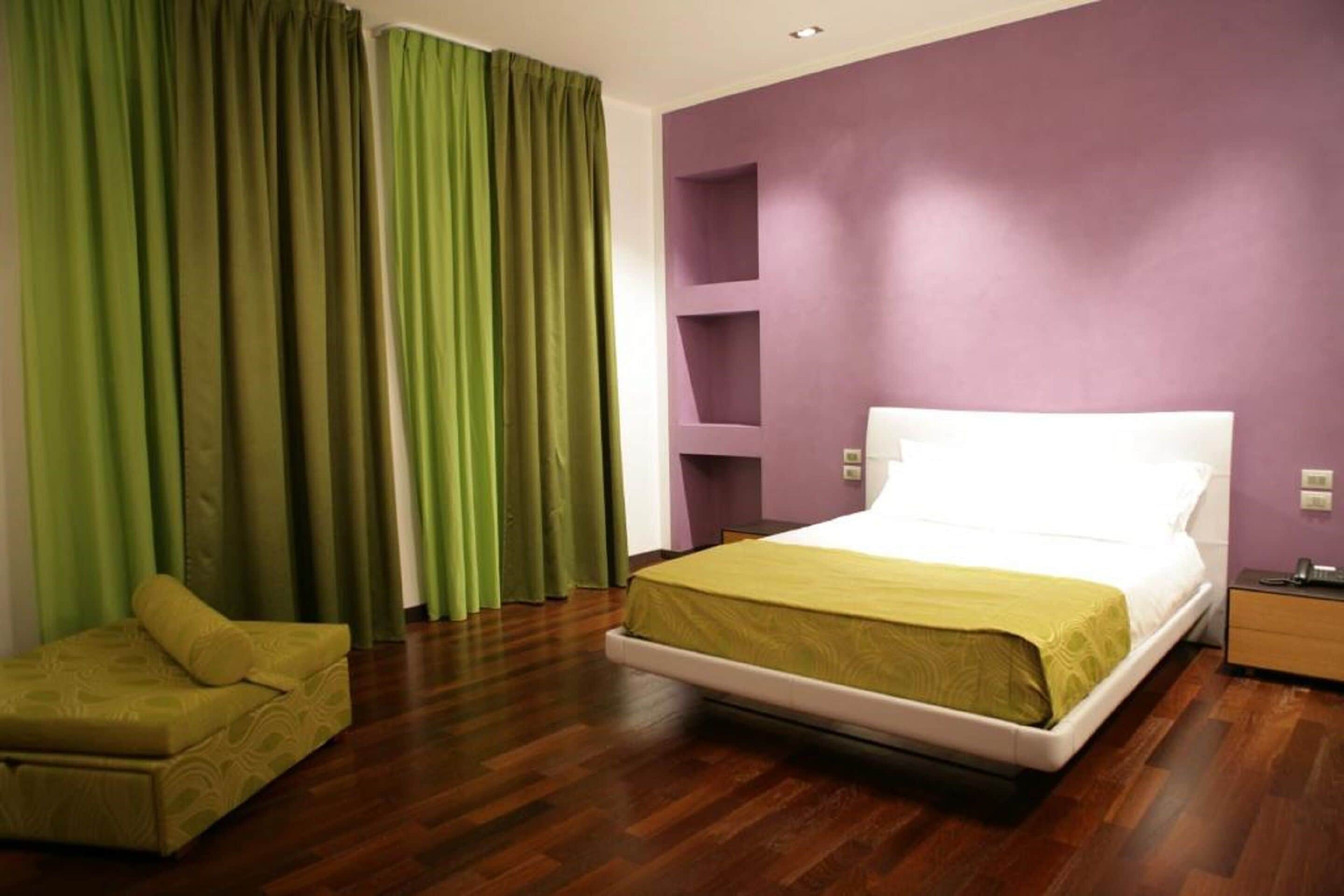A bedroom with a bed, a nightstand, a chair, and a purple wall.