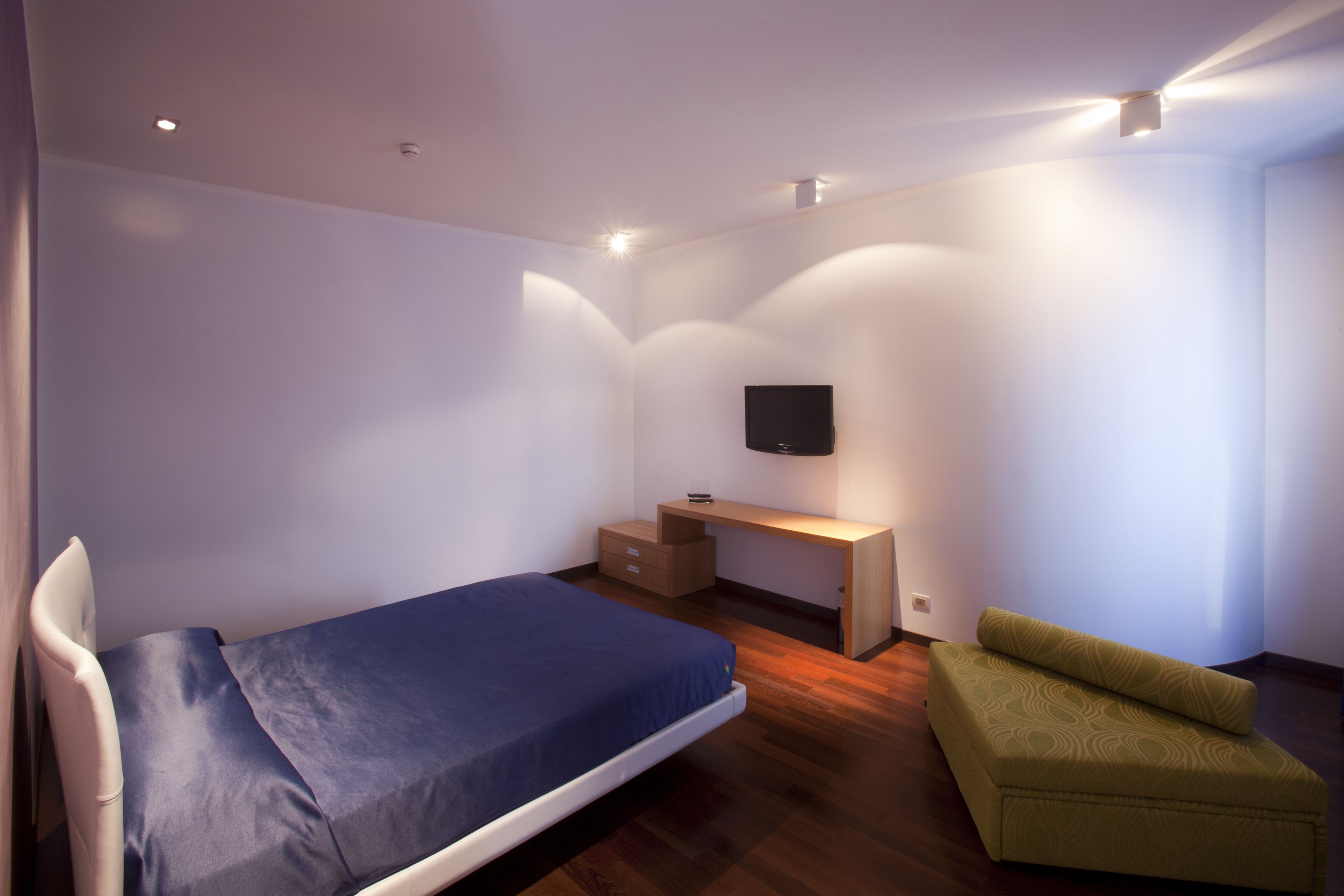 Un dormitorio con cama, escritorio, silla y televisor montado en la pared.