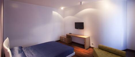 Un dormitorio con cama, escritorio, silla y televisor montado en la pared.