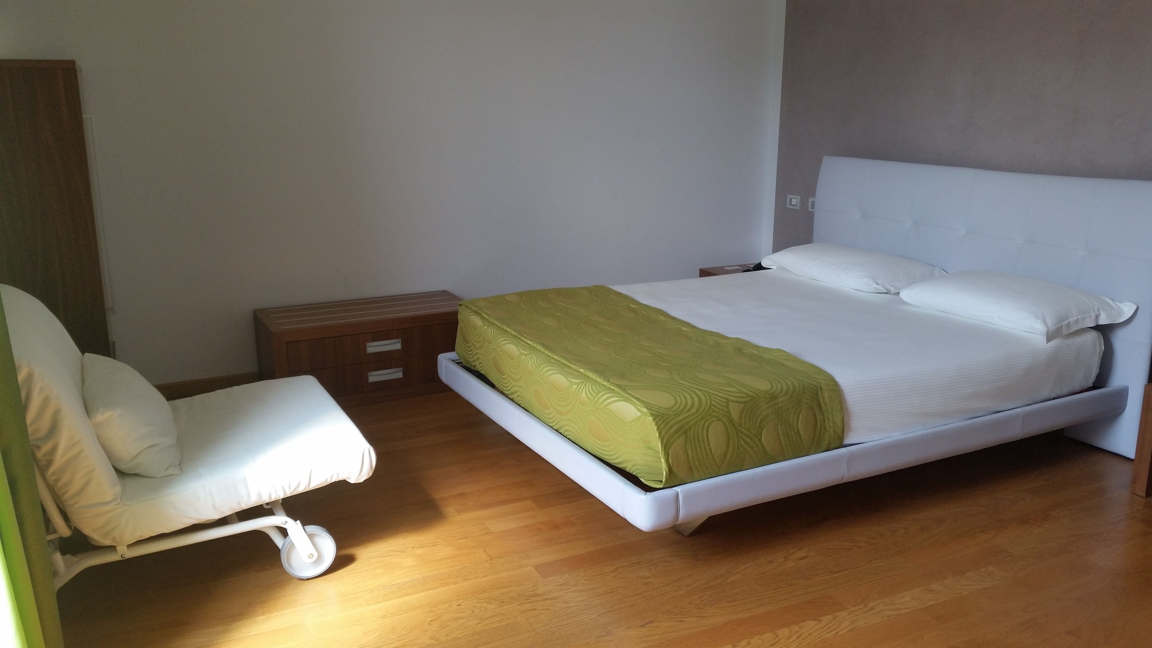 A bedroom with a bed, a chair, a nightstand, and a wooden floor.