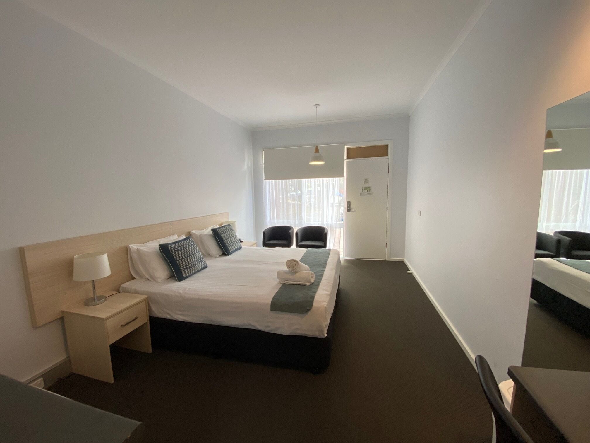 Una habitación de hotel con cama, mesita de noche, lámpara y una silla.