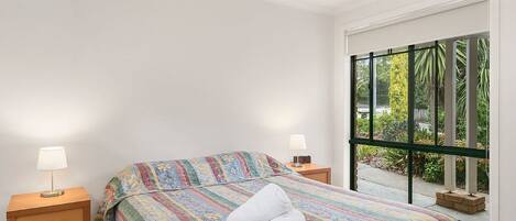 Ein Schlafzimmer mit einem Bett, zwei Nachttischen, einem Fenster mit Blick ins Grüne und einer weißen Wand.