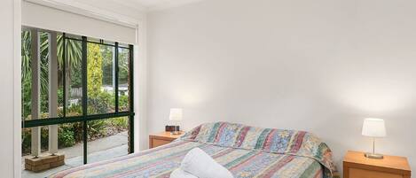 A bedroom with a bed, two bedside tables, and a window with a view of greenery.