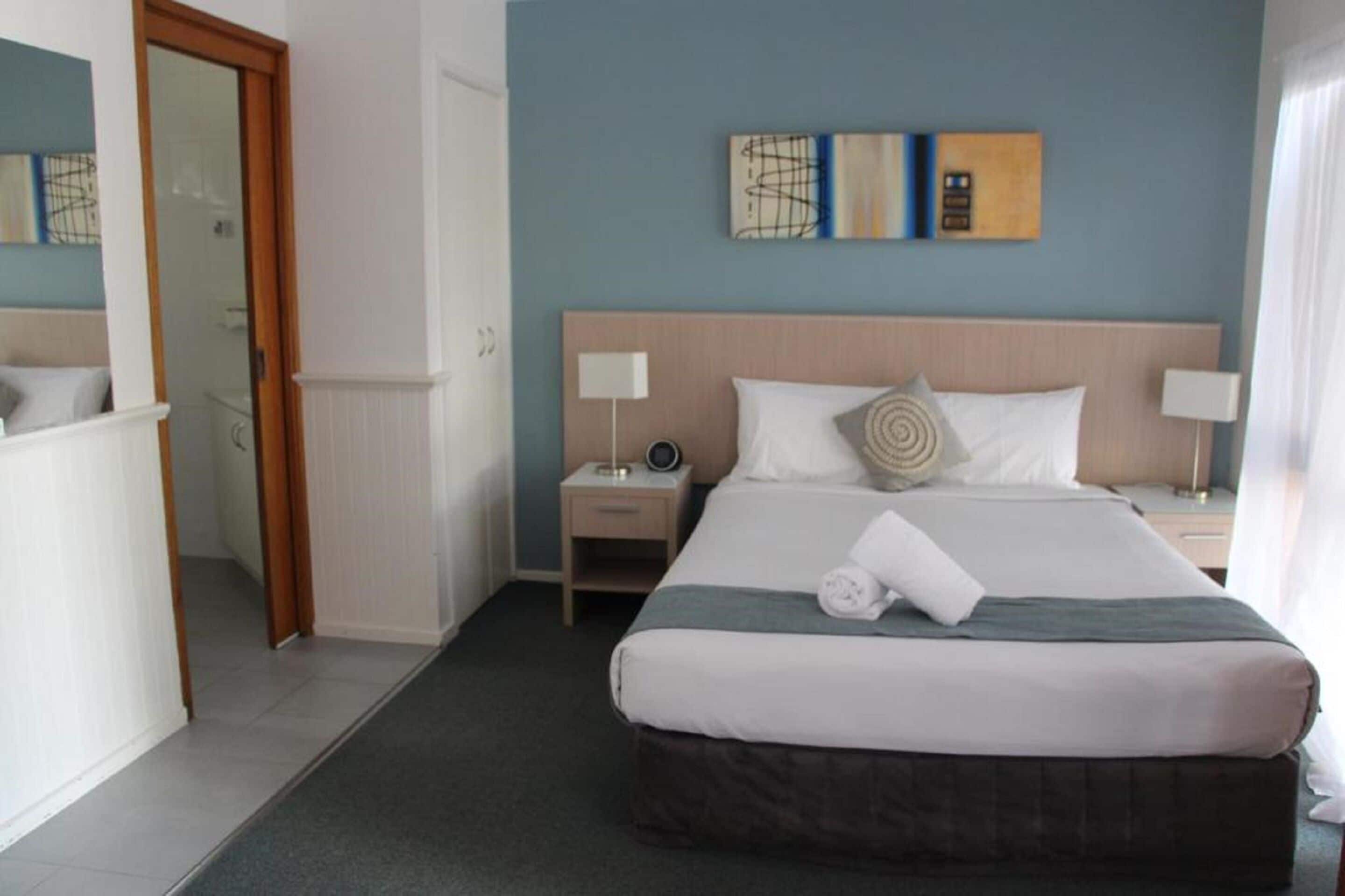 Una camera d'albergo con un letto grande, due comodini e un armadio a muro che conduce al bagno.