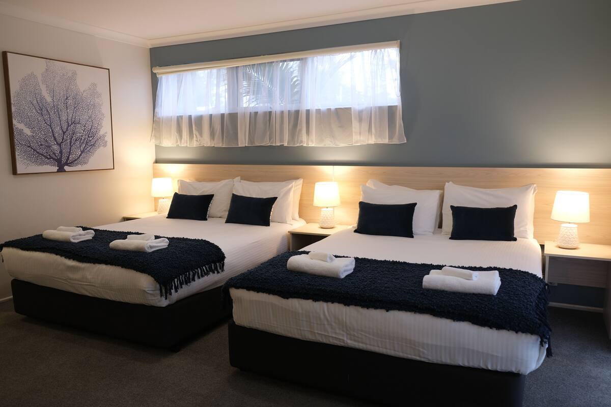 A hotel room with two beds, each with white linens and dark blue throw blankets, and bedside lamps.