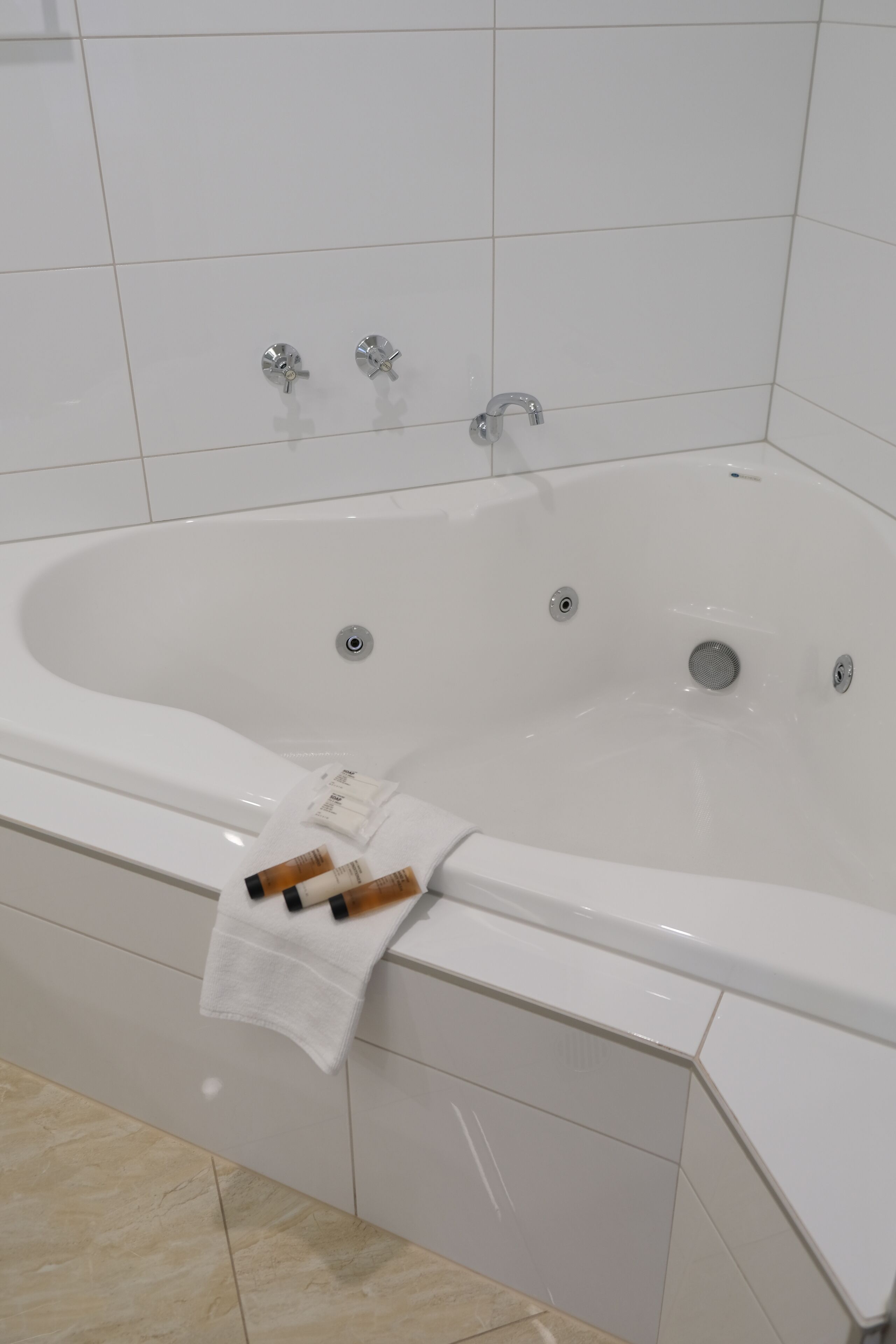 Une baignoire blanche avec deux robinets et un drain, une serviette et un flacon de lotion posés sur le bord.