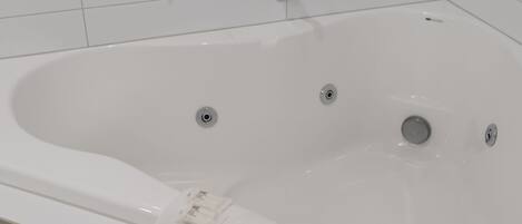 Une baignoire blanche avec deux robinets et un drain, une serviette et un flacon de lotion posés sur le bord.