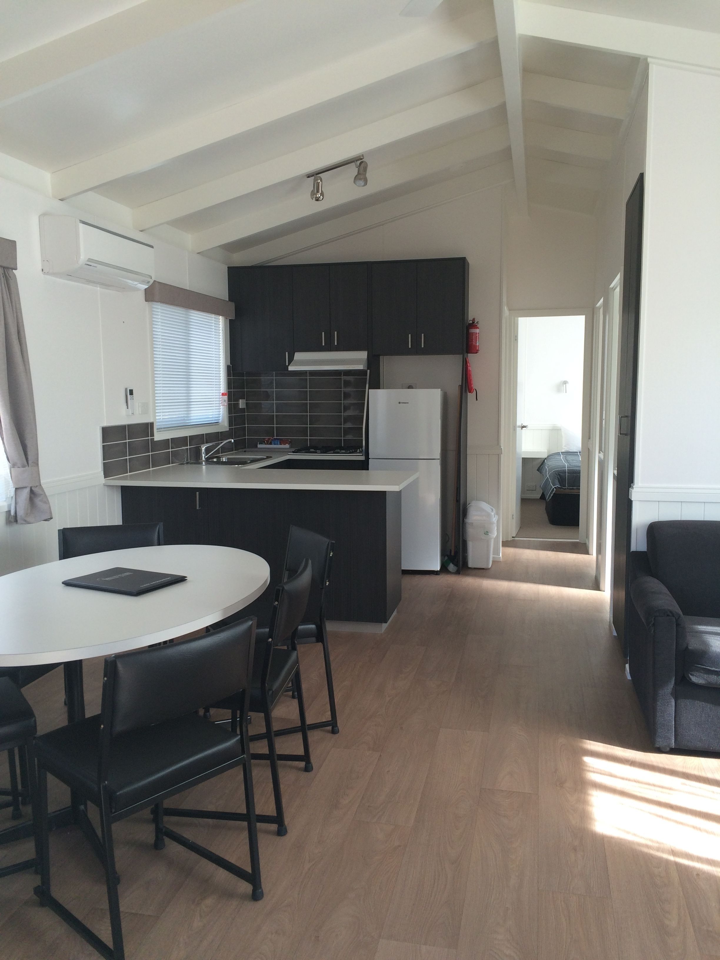 Une cuisine moderne avec des meubles de couleur sombre, un plan de travail blanc et un four encastré. On y trouve également un coin repas avec une table ronde et des chaises.