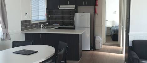 A modern kitchen with dark cabinets, a white countertop, and a built-in oven. There is a dining area with a round table and chairs.