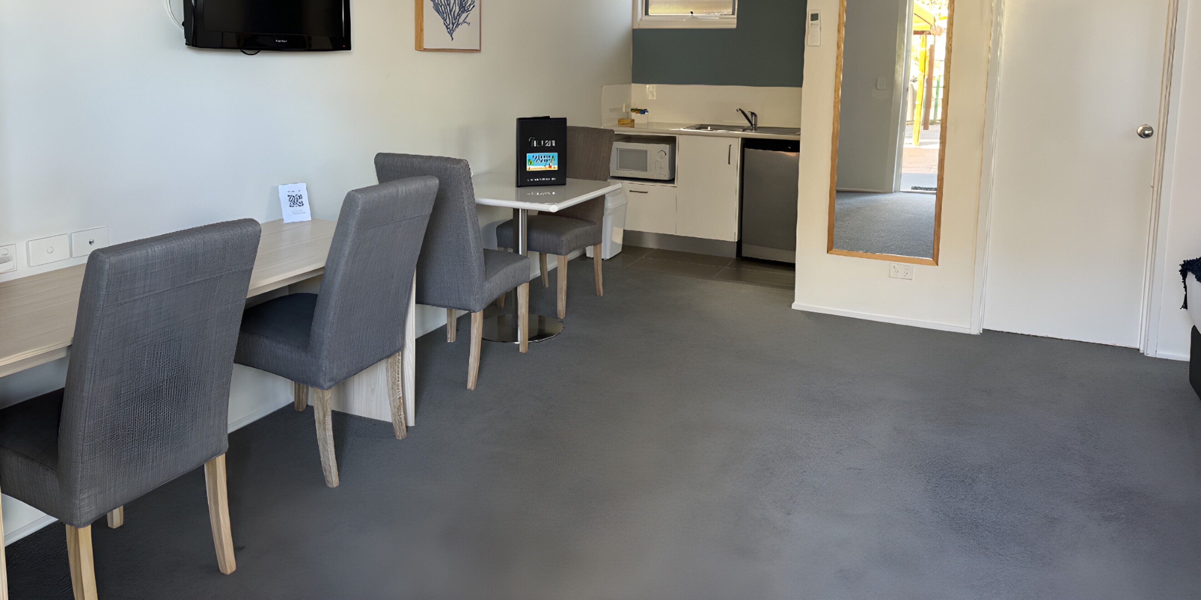 A modern hotel room with a dining area, kitchenette, and a TV mounted on the wall.