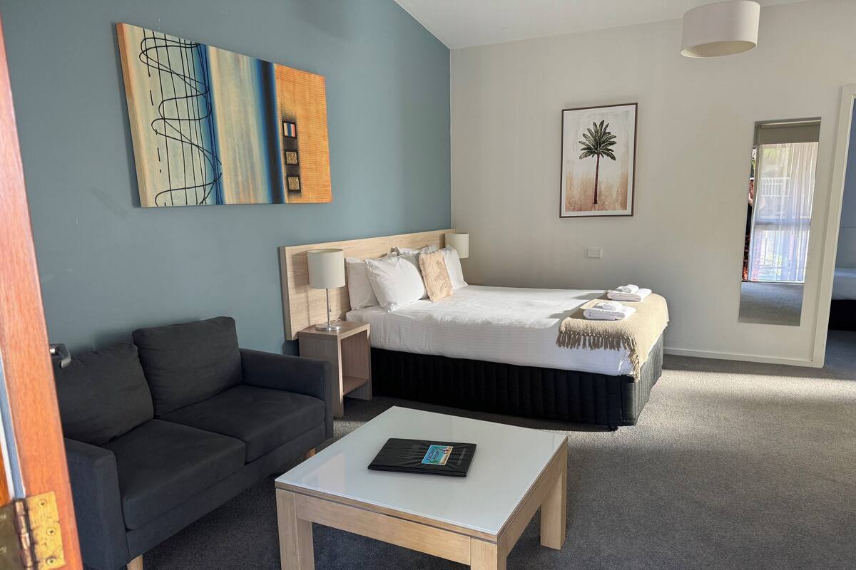 A hotel room with a bed, a sofa, a table, and artwork on the walls.
