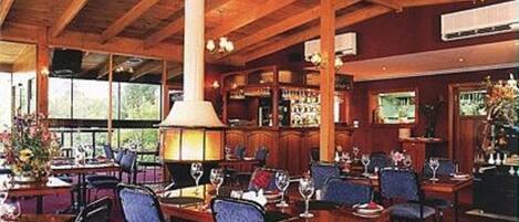 Un restaurante con vigas de madera, mesas con sillas y una chimenea blanca grande.