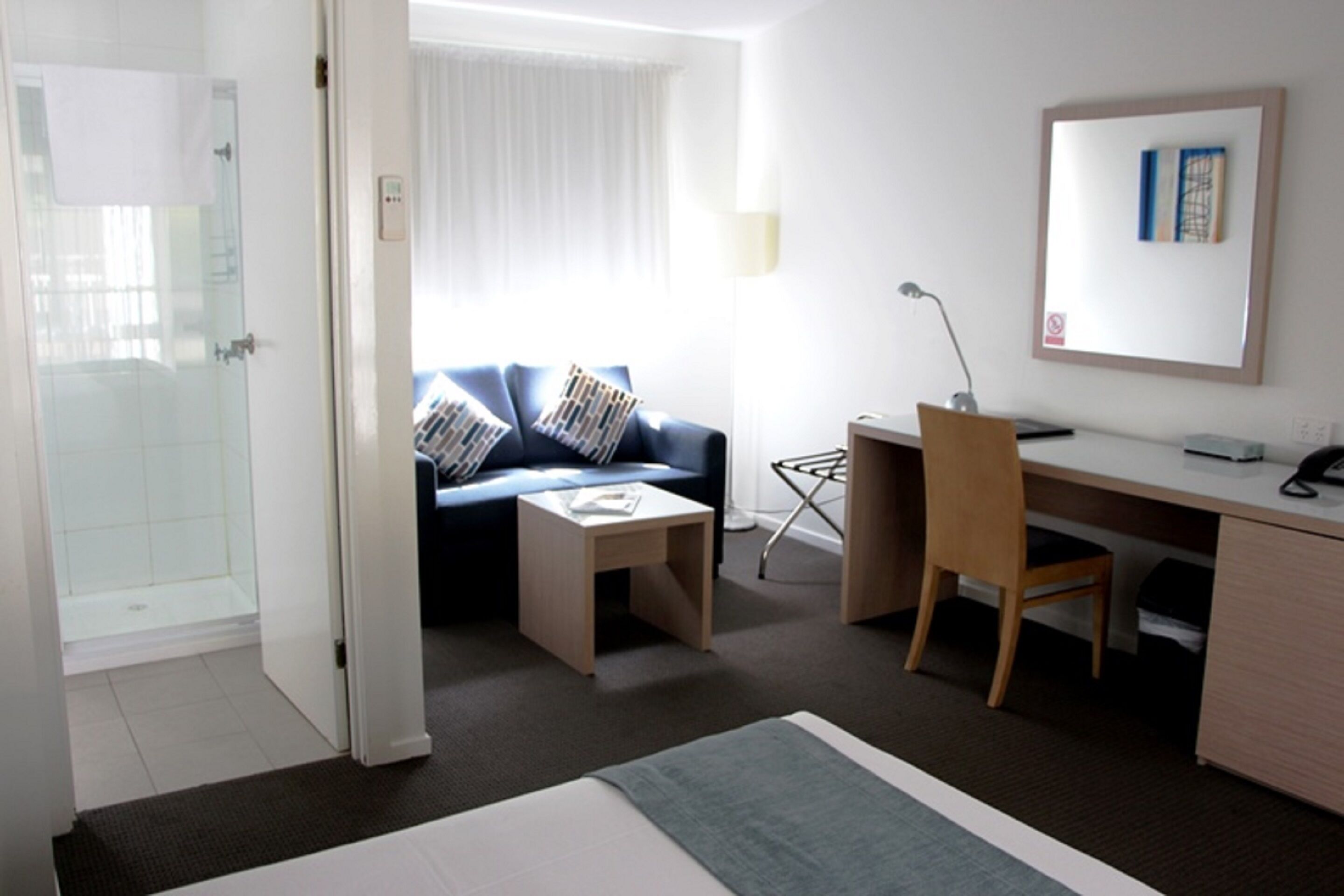 Ein Hotelzimmer mit Bett, Schreibtisch, Stuhl, Sofa, einem kleinen Tisch, einer Lampe und einer Duschkabine.