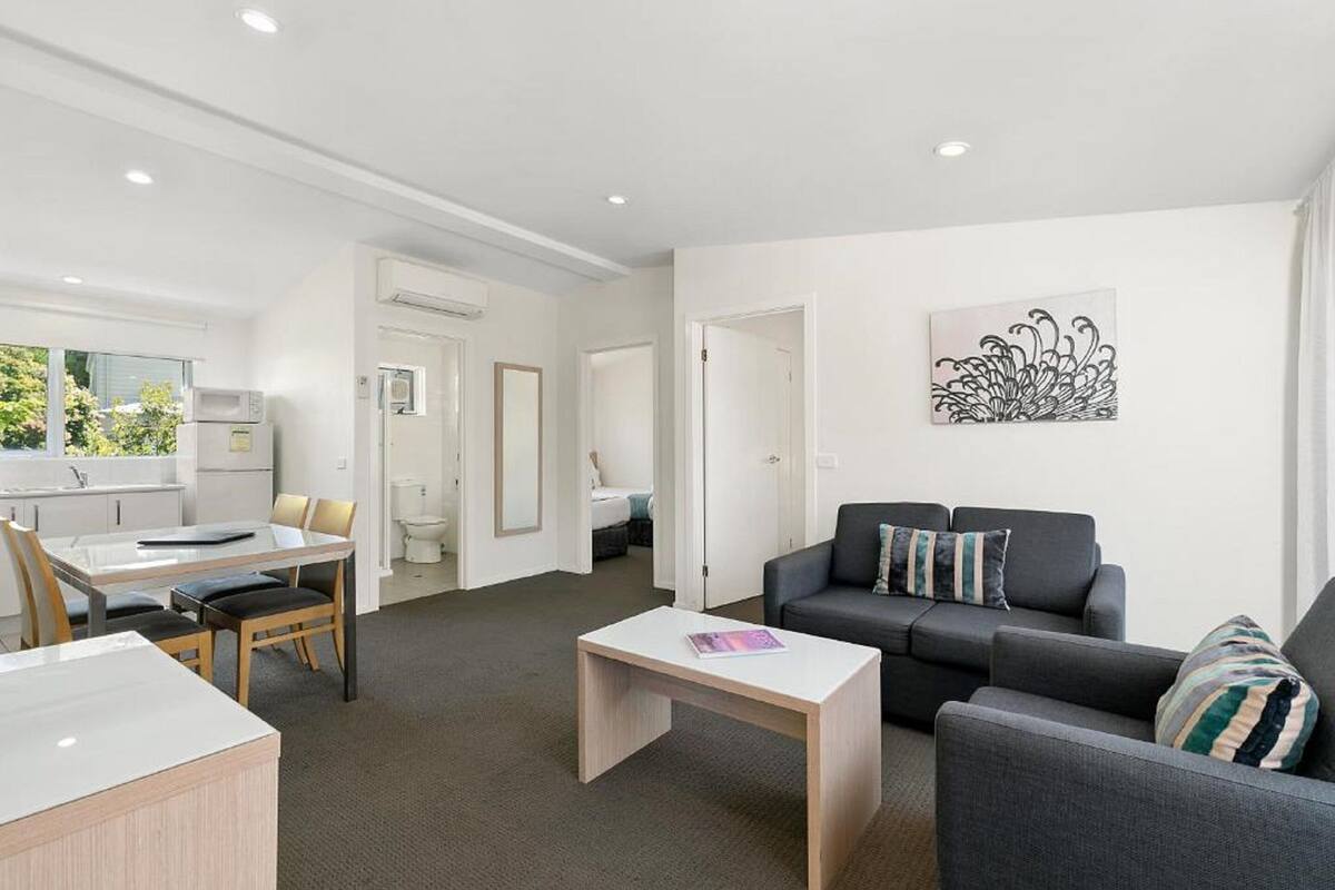 A modern living room with a grey sofa, a white coffee table, and a dining area with a white table and chairs.