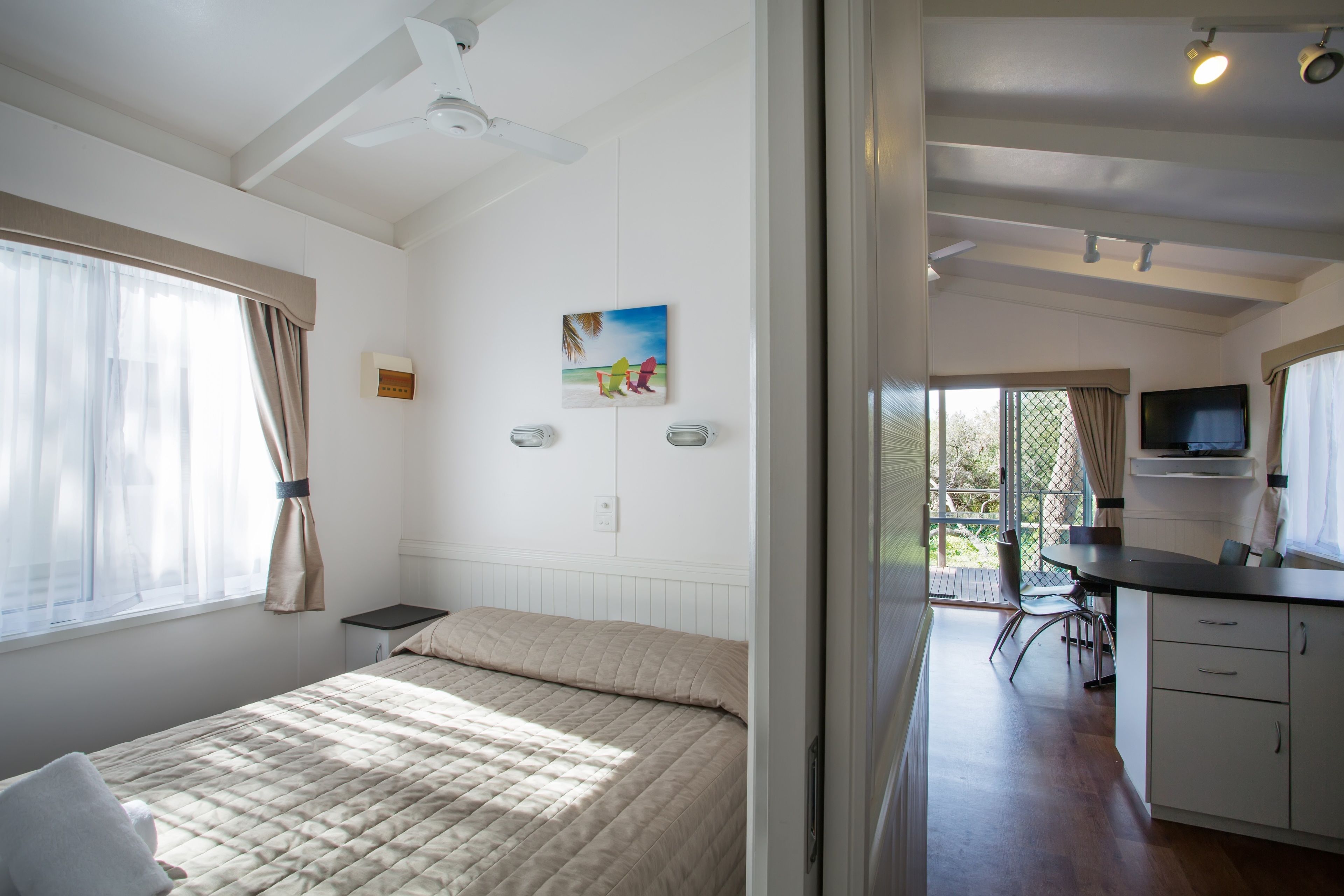 A bedroom with a bed, a desk, and a television in the adjacent room.