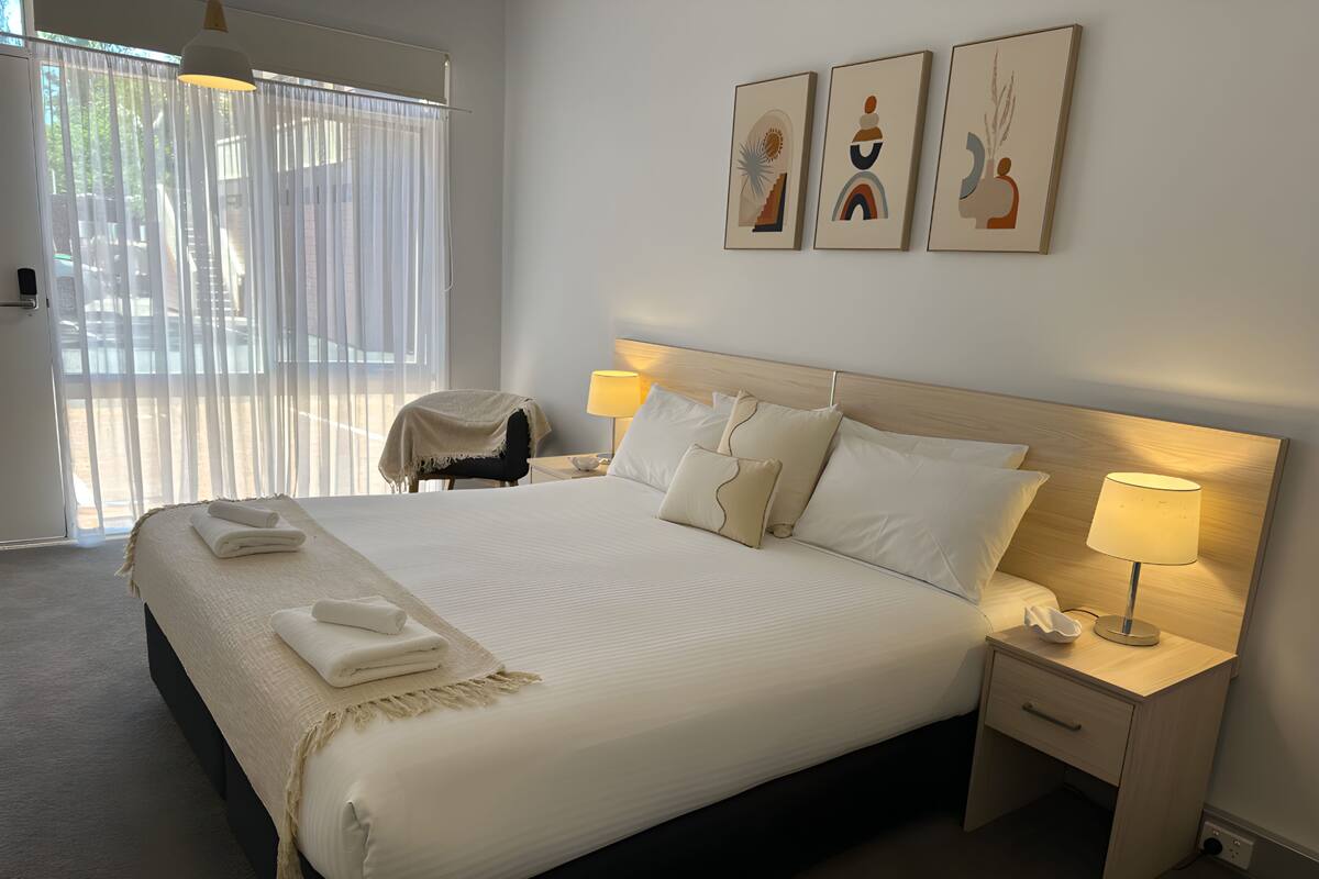 A neatly made bed with white linens, a bedside lamp, and a small bedside table with a lamp.