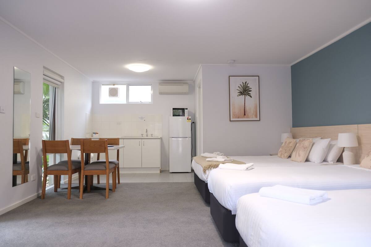 A hotel room with a bed, bedside table, and a small kitchenette.
