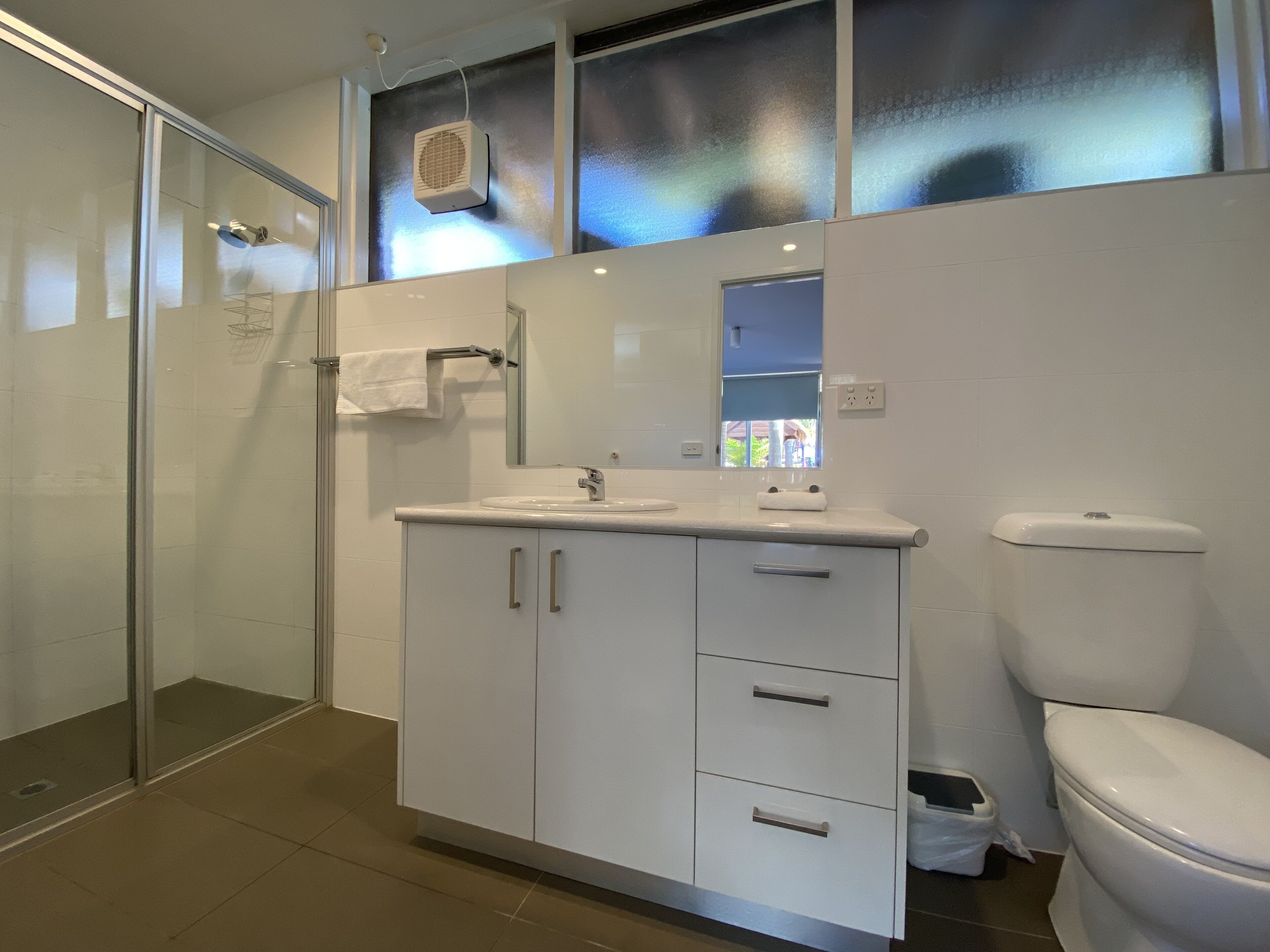 Une salle de bain moderne avec une douche à parois de verre, un lavabo blanc avec un miroir au-dessus et des toilettes.