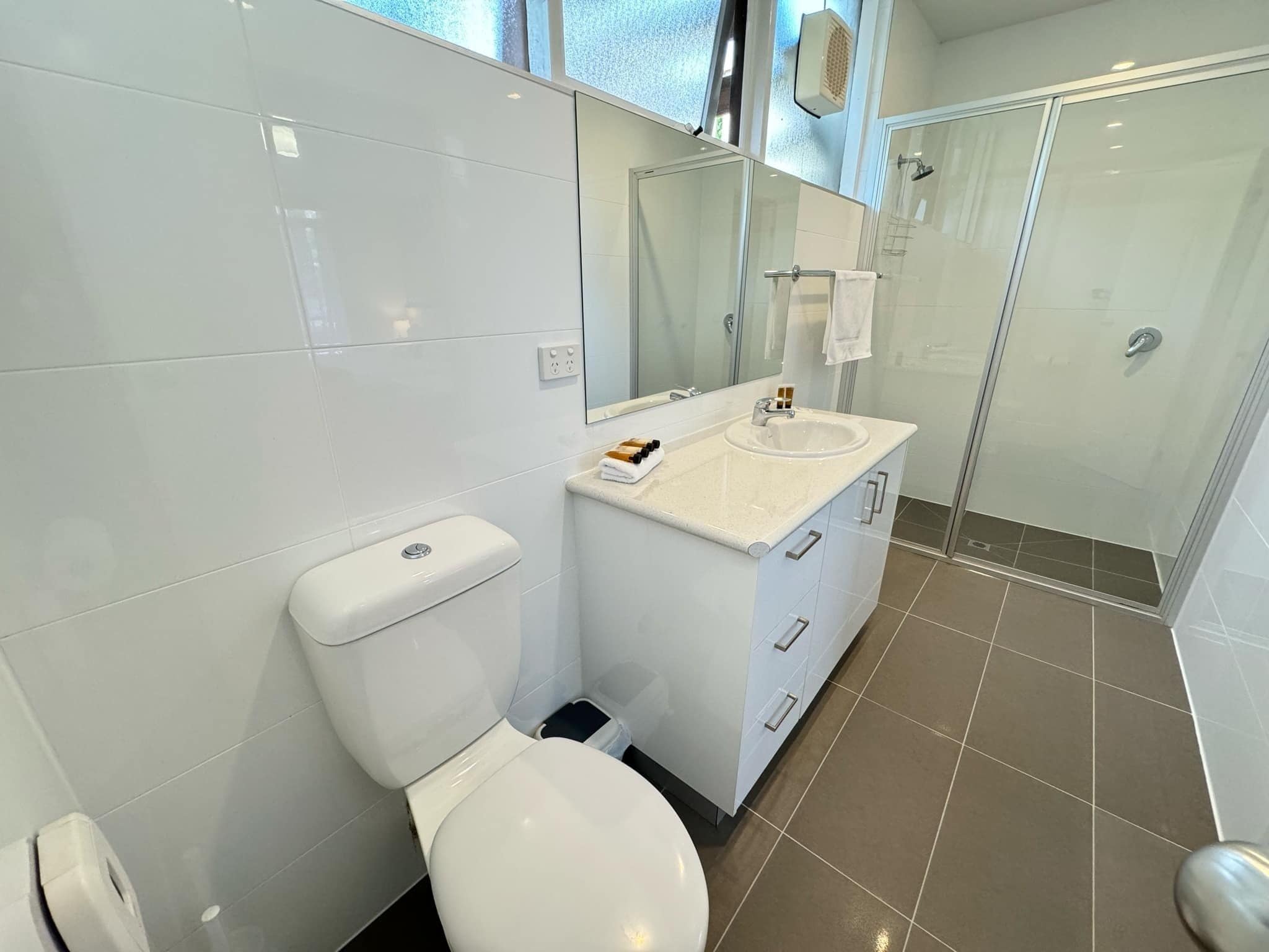 A modern bathroom with a white toilet, a sink with a mirror above it, and a shower area.