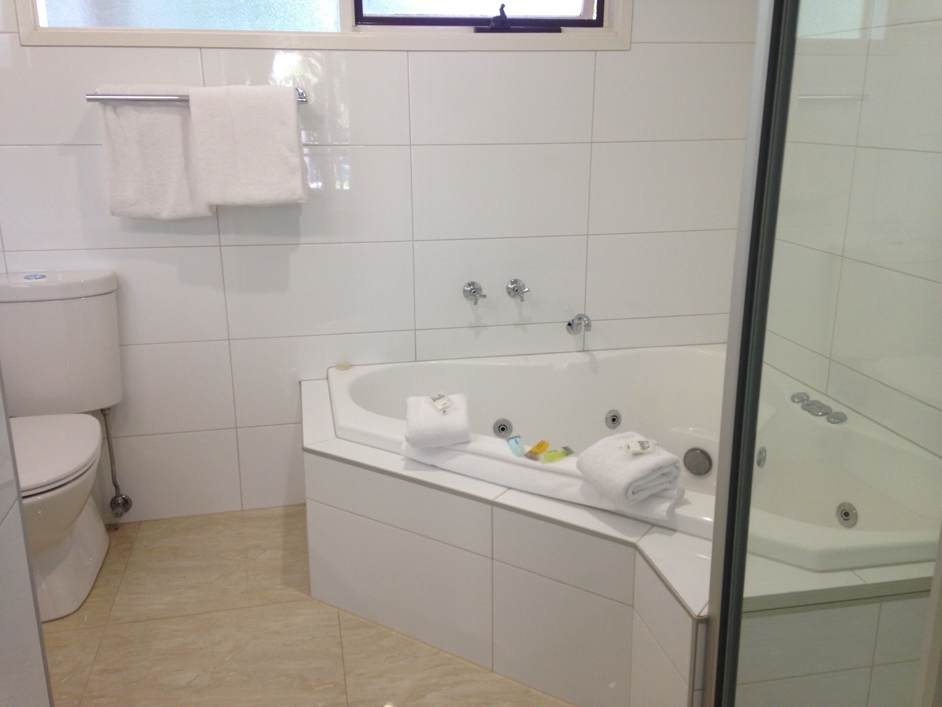 A bathroom with a toilet, a bathtub with a glass enclosure, and a window above the toilet.