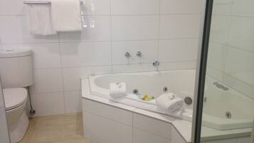 Un baño con inodoro, bañera con mampara de vidrio y ventana sobre el inodoro.