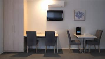 A hotel room with a desk, two chairs, a television, and a framed artwork on the wall.