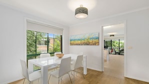 A modern dining area with a white table and chairs, large windows with a view of greenery, and a painting on the wall. - Kaloha Holiday Resort (Cowes)
