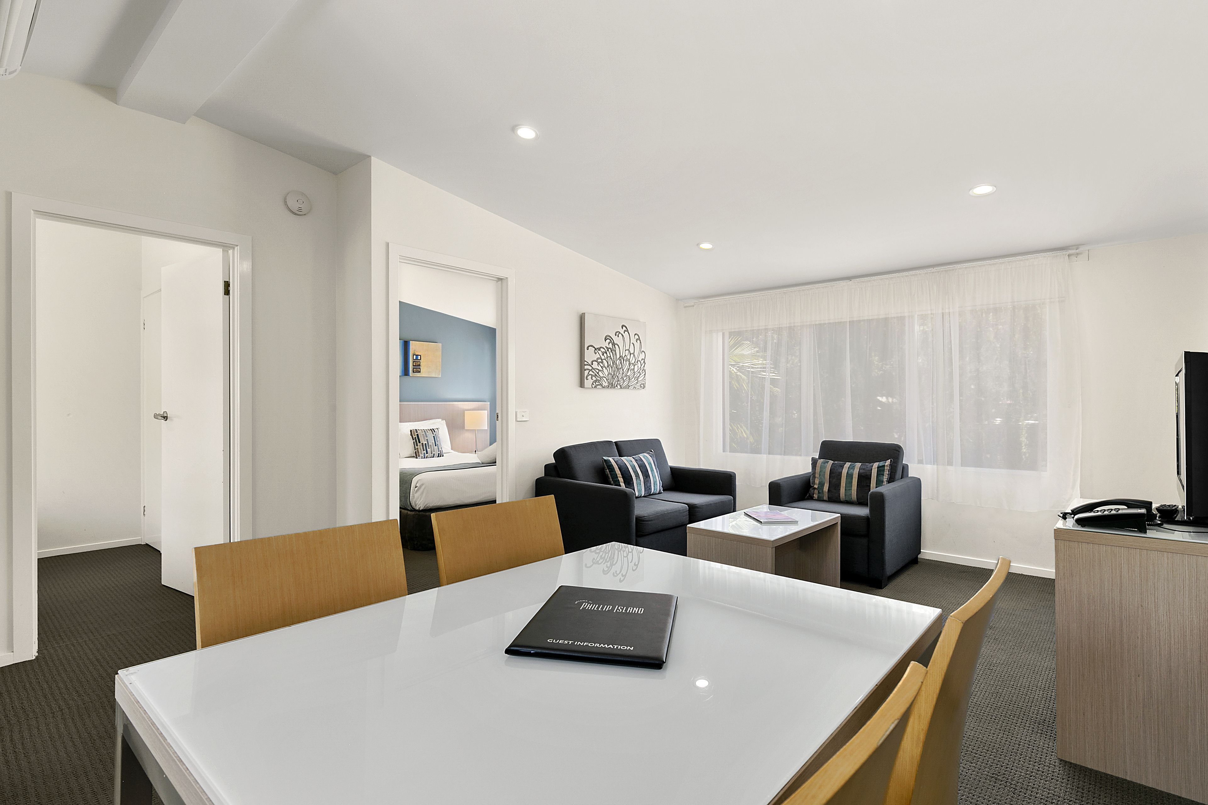 A modern hotel room with a dining area, two sofas, a small table, a desk, and a television.