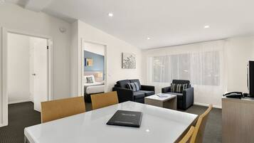 A modern hotel room with a dining area, two sofas, a small table, a desk, and a television.
