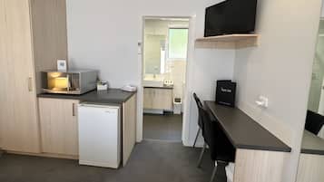 Una cocina compacta con microondas, refrigerador y un lavamanos pequeño. Hay un televisor montado en la pared y una silla en la barra.