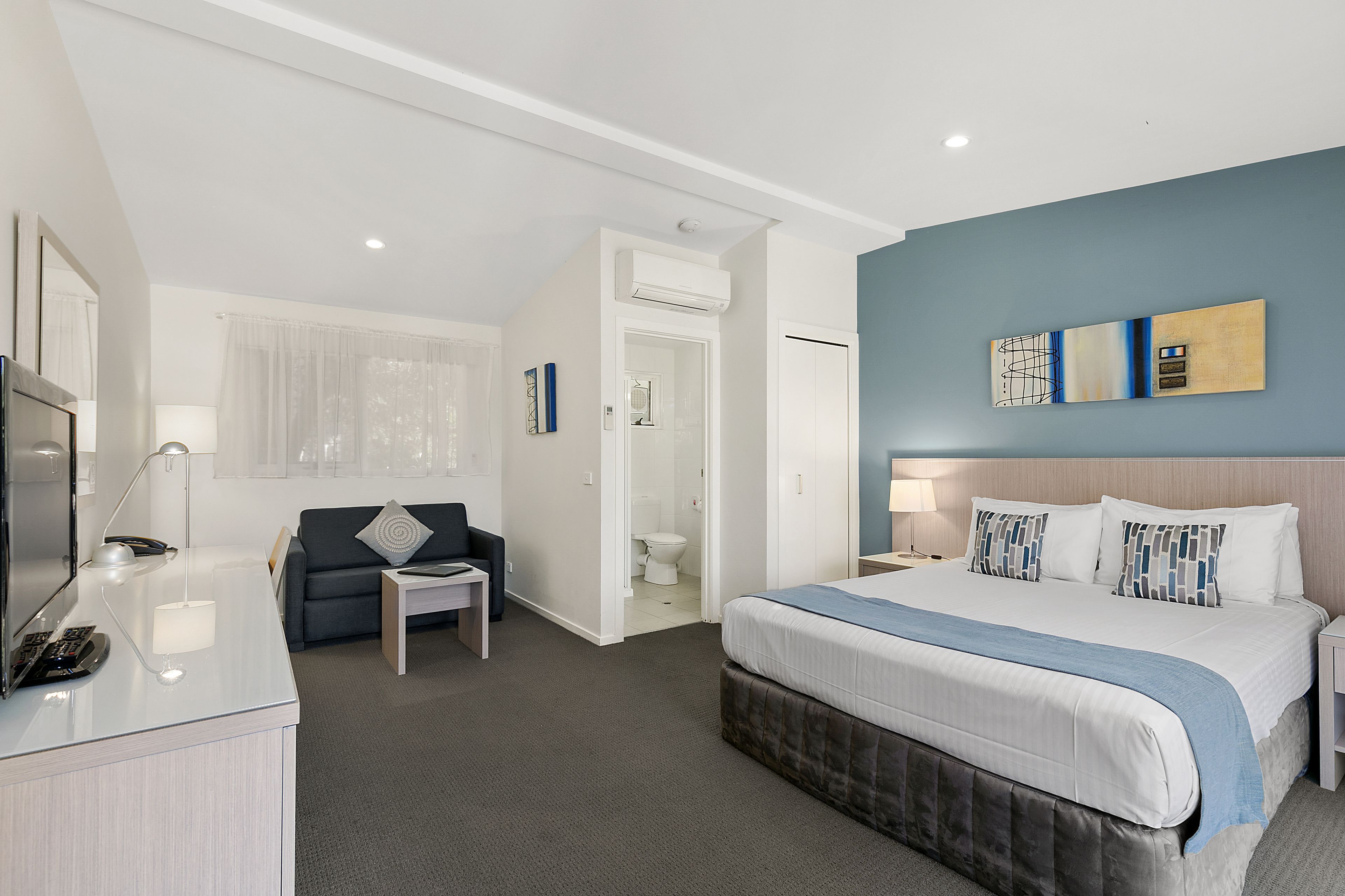 A hotel room with a bed, a desk, a chair, a sofa, and a bathroom.