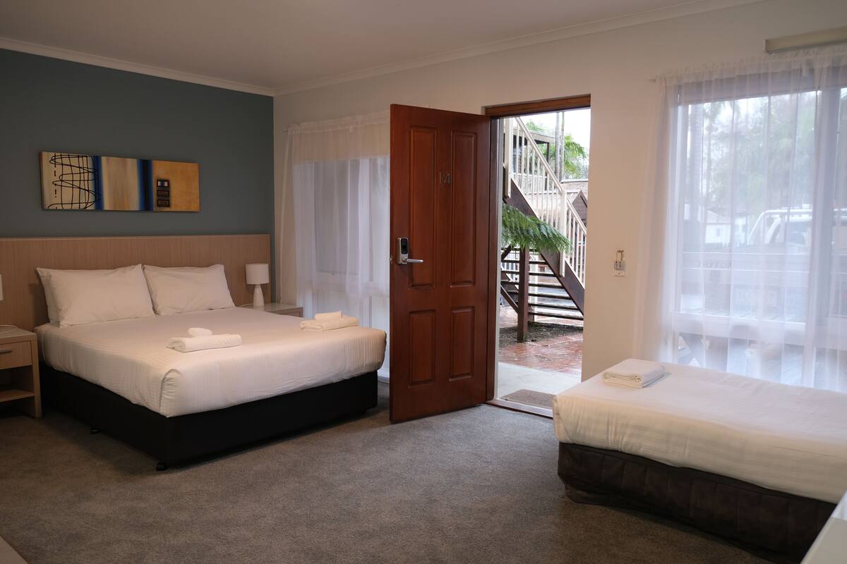 A hotel room with a large bed, a smaller bed, a nightstand, and a door leading to a balcony.