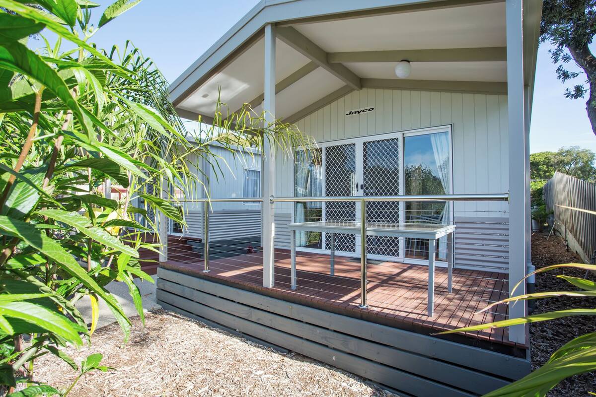 A covered patio area with a table and chairs, surrounded by a wooden deck and a metal railing.