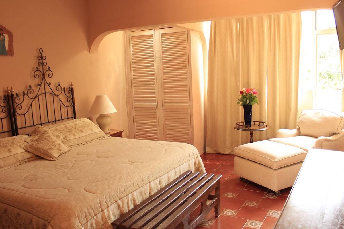 A bedroom with a bed, bedside table, lamp, chair, and a window with curtains.