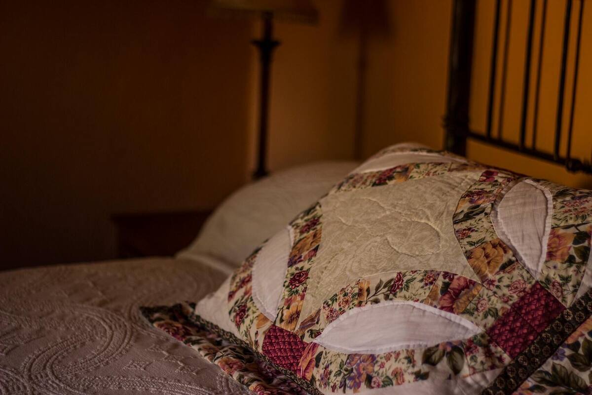 A bed with a floral-patterned quilt and a plain pillow.