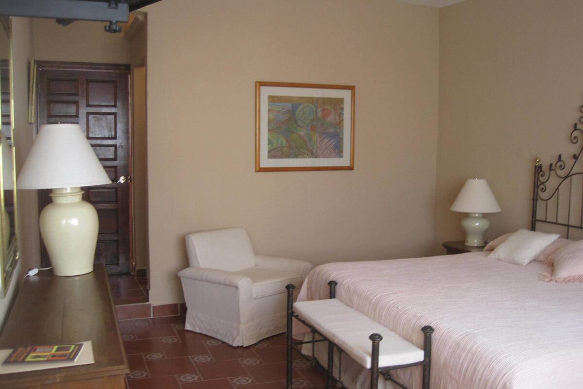A bedroom with a bed, two bedside tables with lamps, a chair, and a bench.