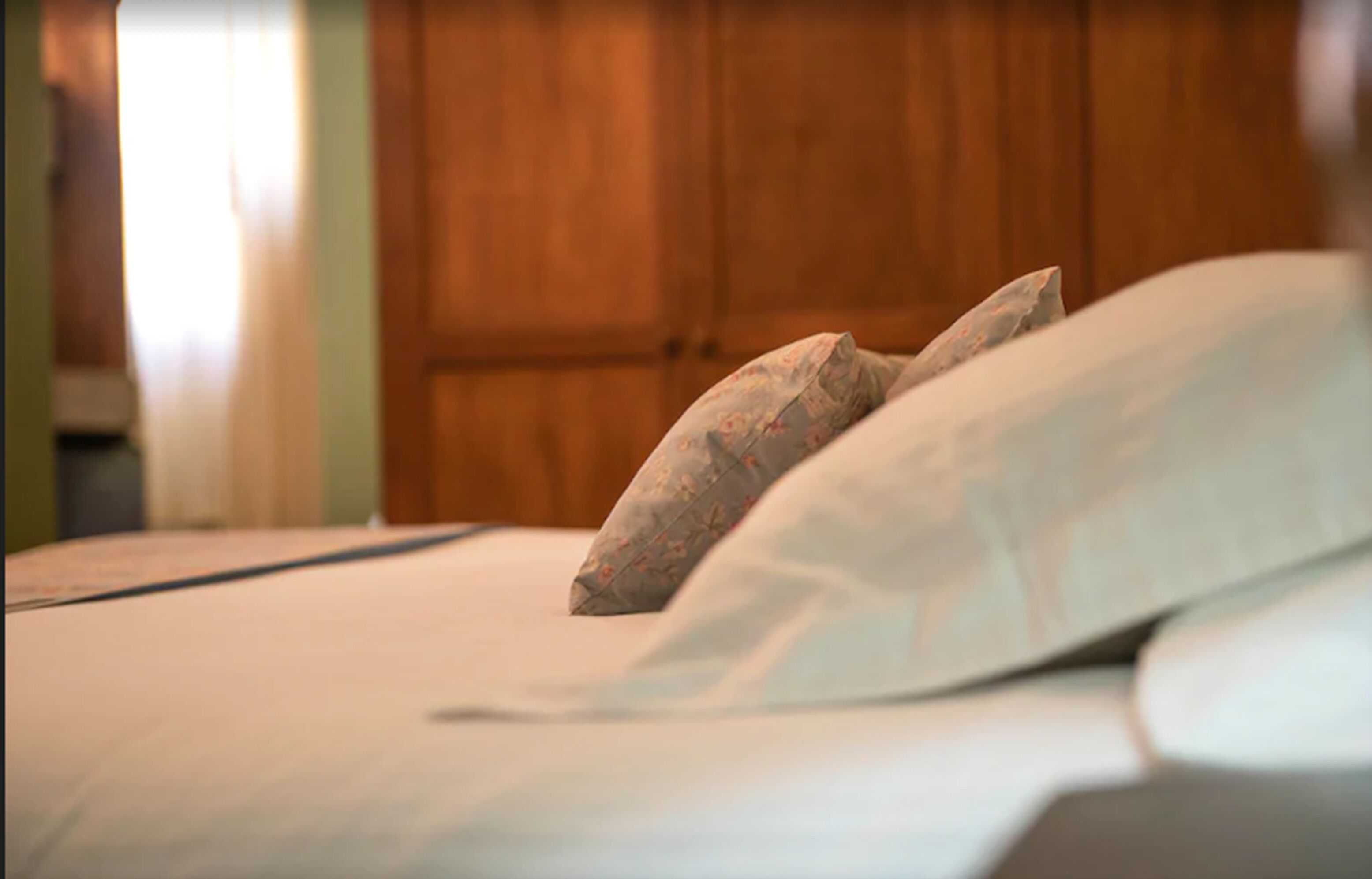 A bed with white bedding and a floral pillow.