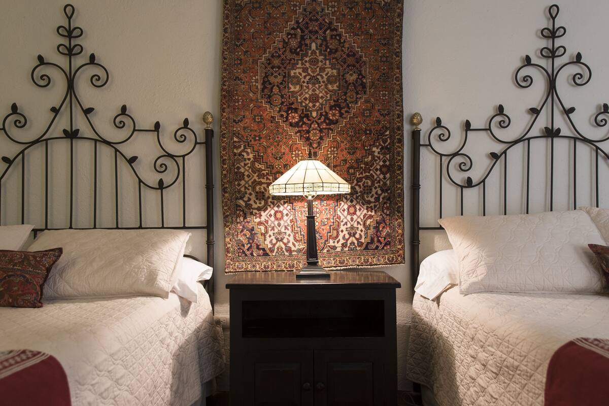 A room with two beds, a patterned rug, and a lamp on a nightstand.