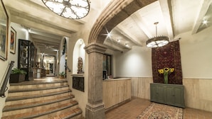 A grand staircase leading to a hallway with a large chandelier, a patterned rug, and a decorative wall panel. - Villa Mirasol Hotel (San Miguel de Allende)