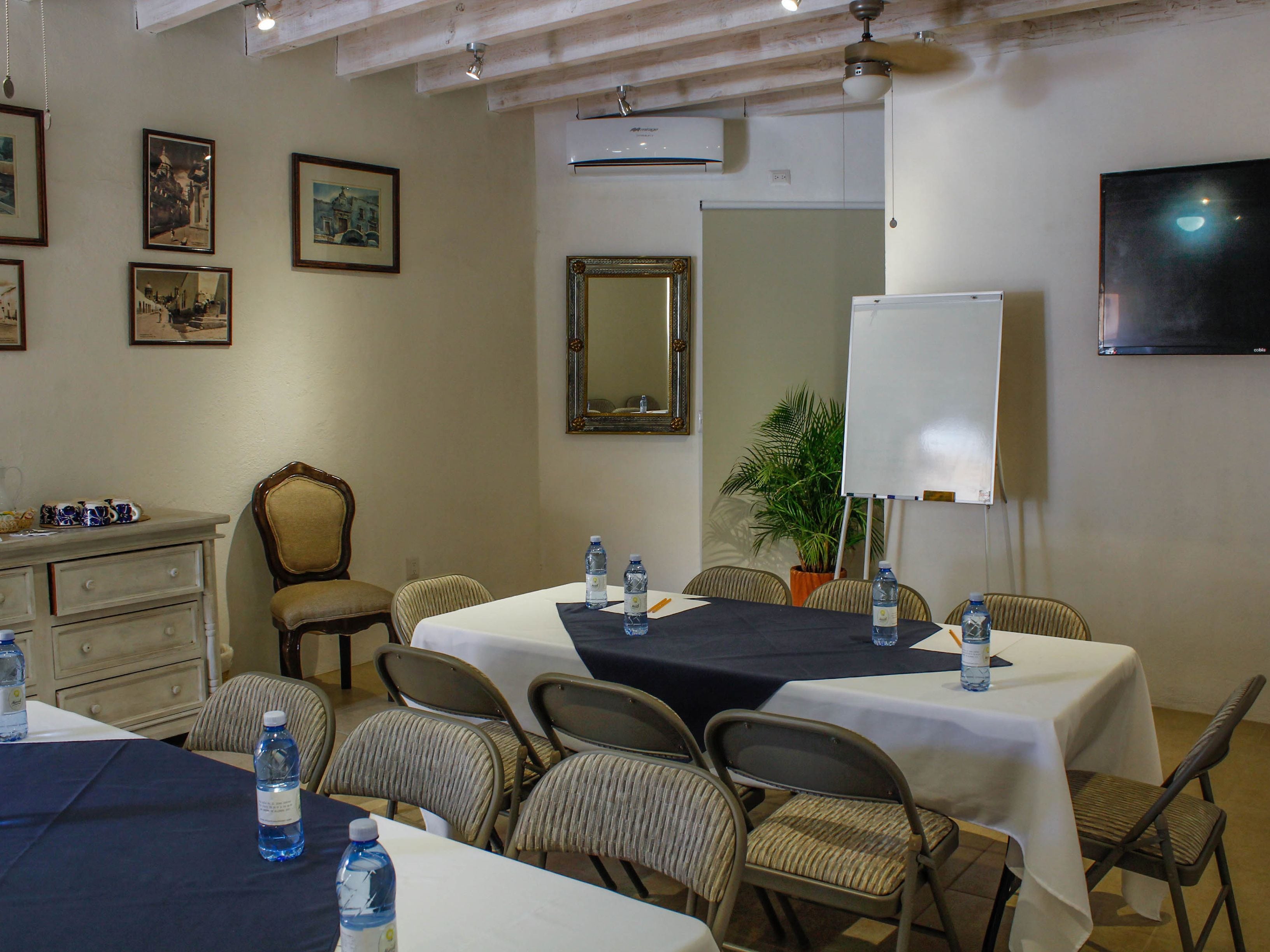 A conference room with tables, chairs, framed pictures, a whiteboard, and a television.