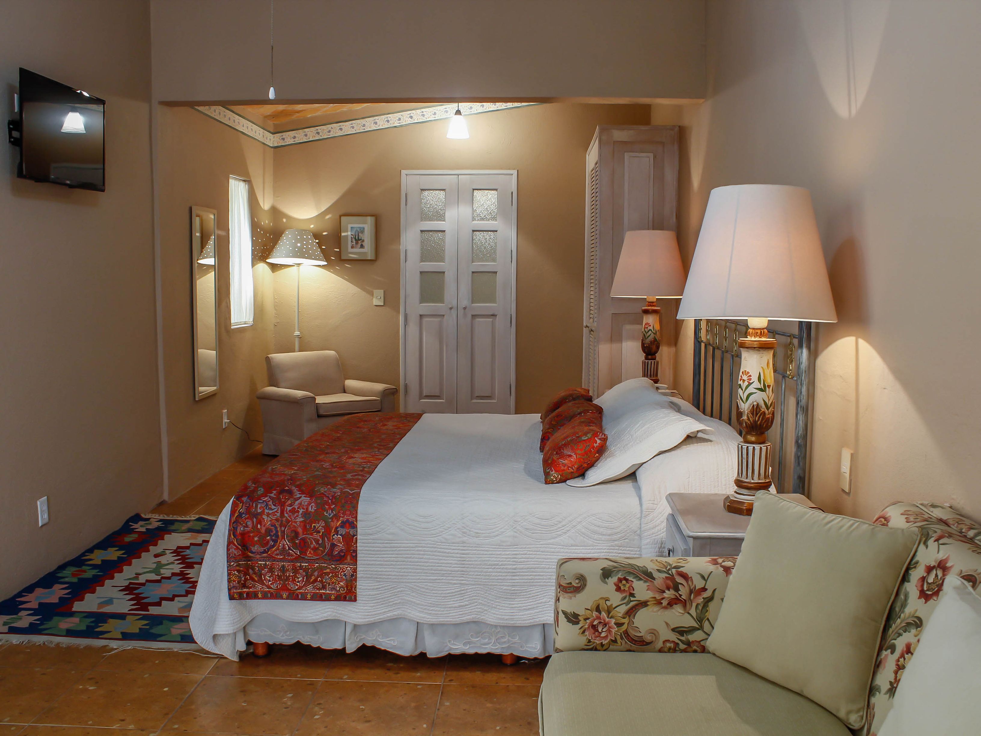 Un dormitorio con cama, una silla, un sofá, una lámpara y un televisor.
