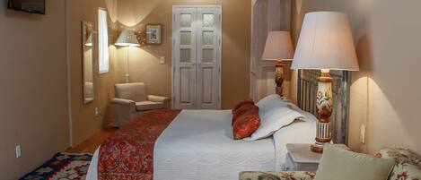 Un dormitorio con cama, una silla, un sofá, una lámpara y un televisor.